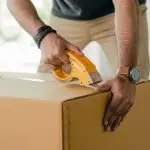 crop man taping carrying box with scotch